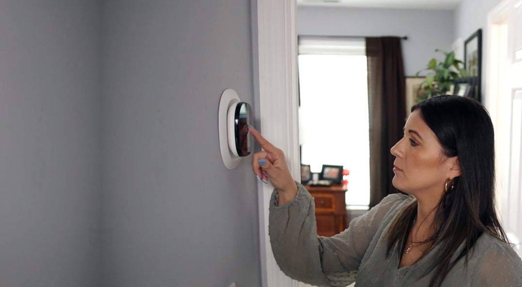 woman adjusting digital thermostat on wall