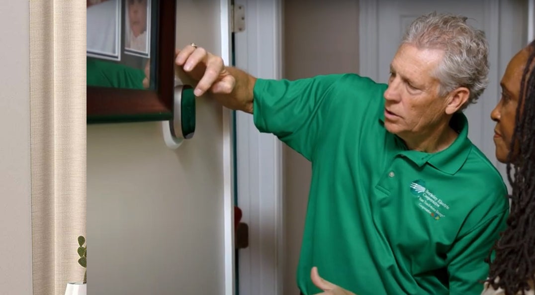 Man wearing green polo showing woman how to work a smart thermostat