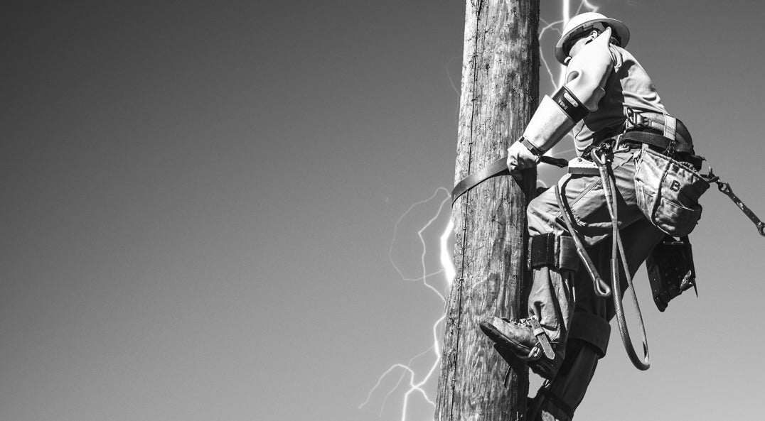 black and white photo of lineman climbing wooden power pole