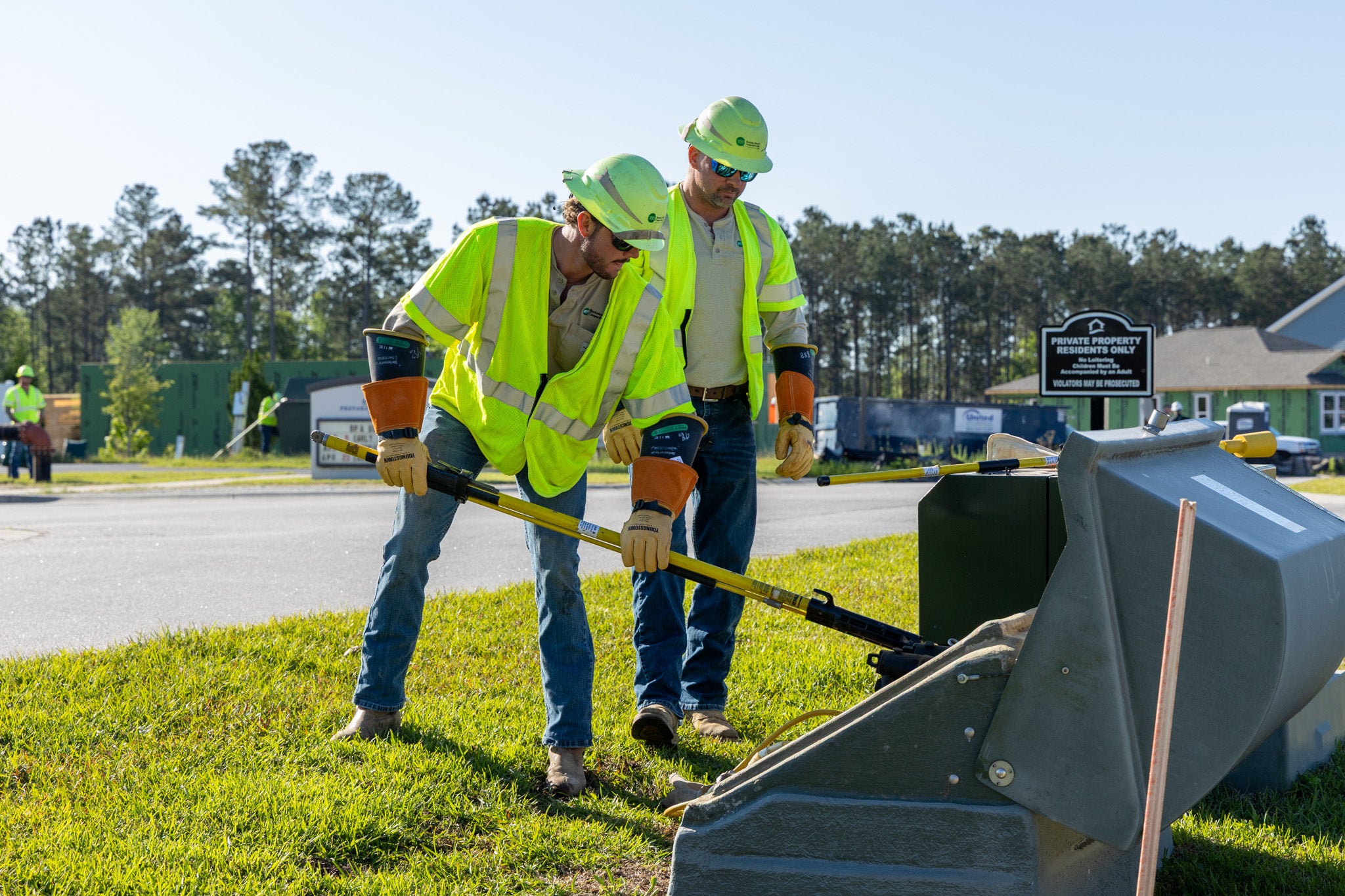 Two linemen using a yellow fiberglass pole to pull fuses inside a padmount transformer.