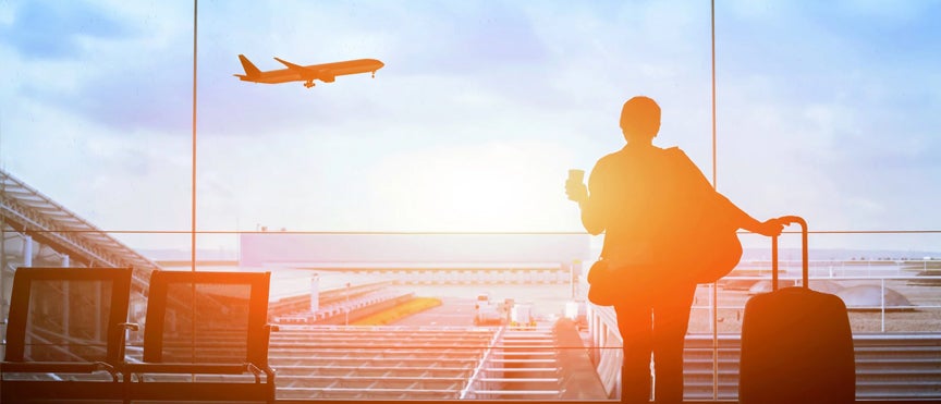 man standing in airport terminal watching a jet take off